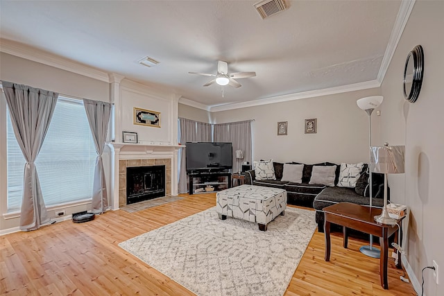 living area featuring ornamental molding, a tile fireplace, visible vents, and light wood finished floors