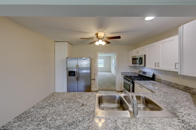 kitchen with ceiling fan, light stone counters, stainless steel appliances, a sink, and white cabinetry