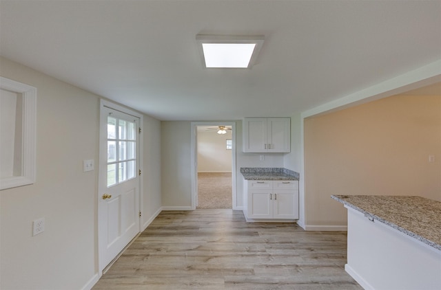 kitchen featuring light wood finished floors, baseboards, white cabinetry, and light stone counters