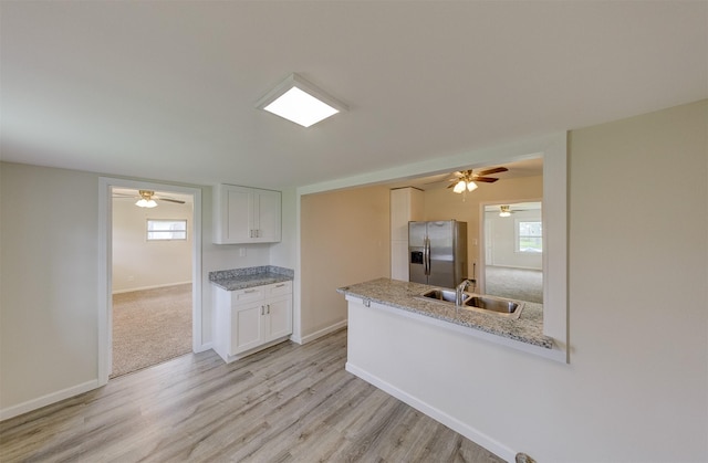 kitchen featuring plenty of natural light, stainless steel refrigerator with ice dispenser, a sink, and white cabinetry