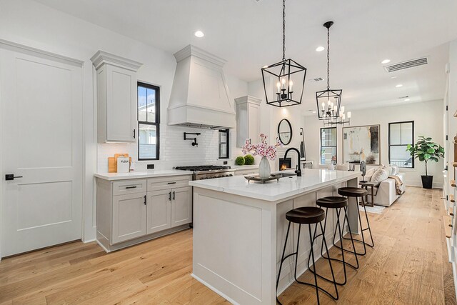 kitchen with light wood-type flooring, light countertops, premium range hood, and decorative backsplash