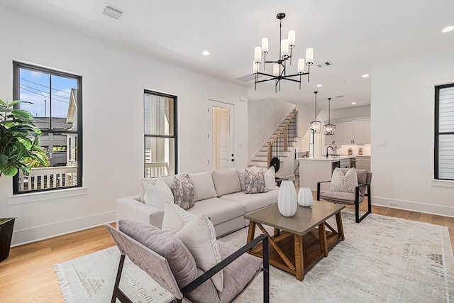 living room featuring light wood-style floors, stairway, visible vents, and a chandelier