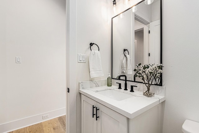 half bath with toilet, baseboards, wood finished floors, and vanity