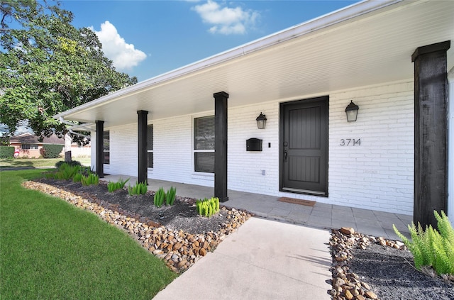 entrance to property with brick siding, covered porch, and a lawn