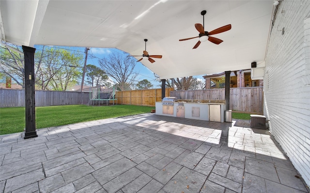 view of patio / terrace with exterior kitchen, a fenced backyard, ceiling fan, a trampoline, and a grill