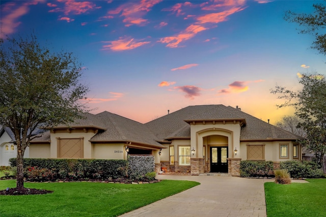 view of front facade featuring driveway, stucco siding, a lawn, and french doors