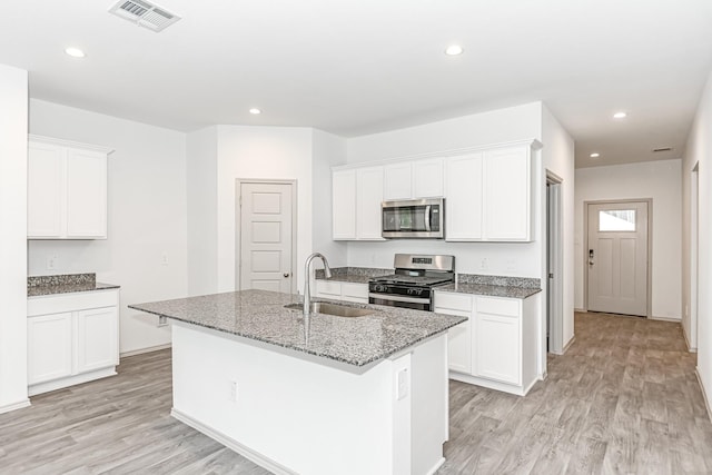 kitchen featuring stainless steel appliances, a sink, visible vents, light wood-style floors, and an island with sink