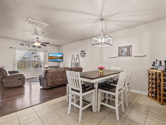 dining space featuring ceiling fan with notable chandelier, visible vents, baseboards, and light tile patterned floors