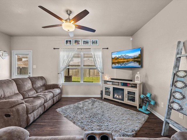 living room with ceiling fan, wood finished floors, a glass covered fireplace, and baseboards