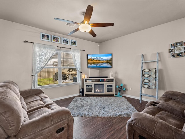 living area featuring dark wood-style floors, visible vents, a glass covered fireplace, ceiling fan, and baseboards