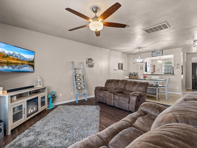 living room featuring baseboards, visible vents, wood finished floors, and a glass covered fireplace