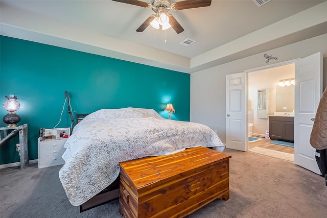 carpeted bedroom with ensuite bathroom, baseboards, visible vents, and a ceiling fan