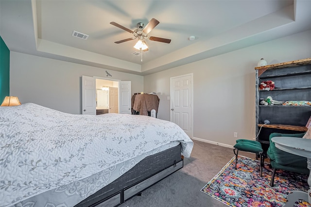 bedroom featuring a ceiling fan, visible vents, baseboards, a tray ceiling, and dark carpet