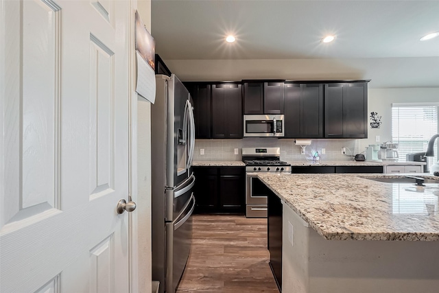 kitchen with stainless steel appliances, tasteful backsplash, wood finished floors, a sink, and light stone countertops