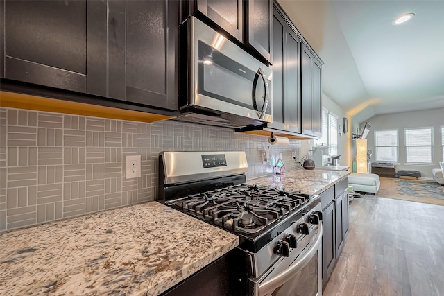 kitchen with light stone counters, stainless steel appliances, decorative backsplash, light wood-style floors, and open floor plan