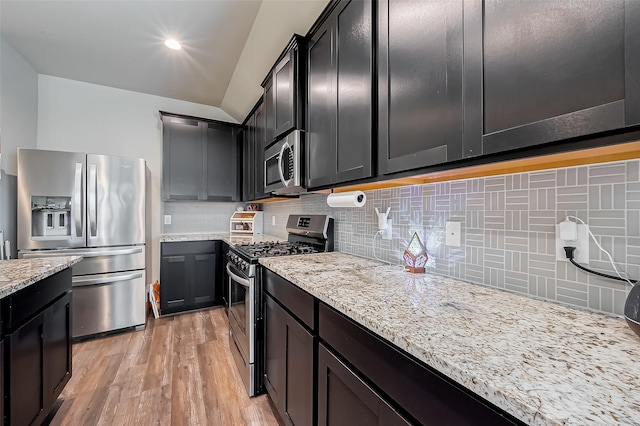 kitchen with light stone counters, dark cabinets, stainless steel appliances, light wood-style floors, and backsplash