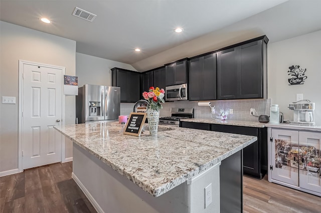 kitchen with tasteful backsplash, visible vents, appliances with stainless steel finishes, wood finished floors, and light stone countertops