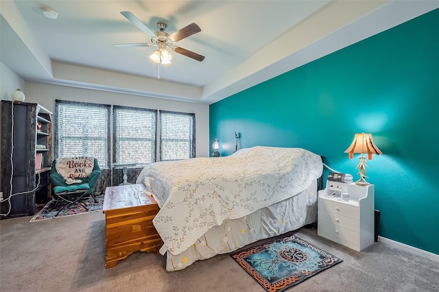 bedroom with ceiling fan, a tray ceiling, and carpet