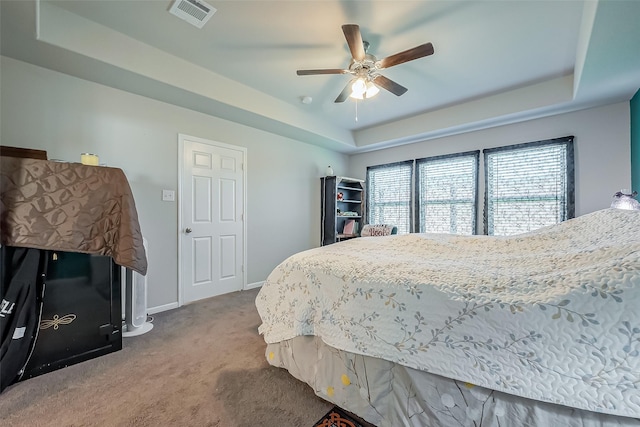 carpeted bedroom featuring a ceiling fan, a raised ceiling, visible vents, and baseboards