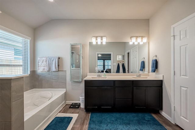 full bathroom with a bath, double vanity, a sink, and wood finished floors