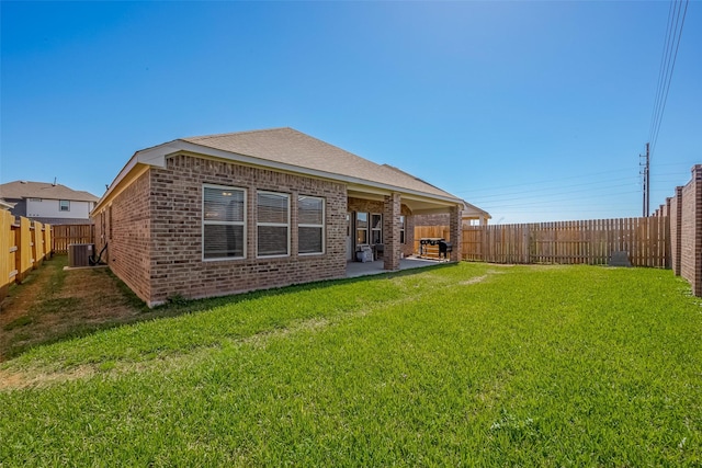 rear view of property featuring central AC unit, a lawn, a patio, a fenced backyard, and brick siding