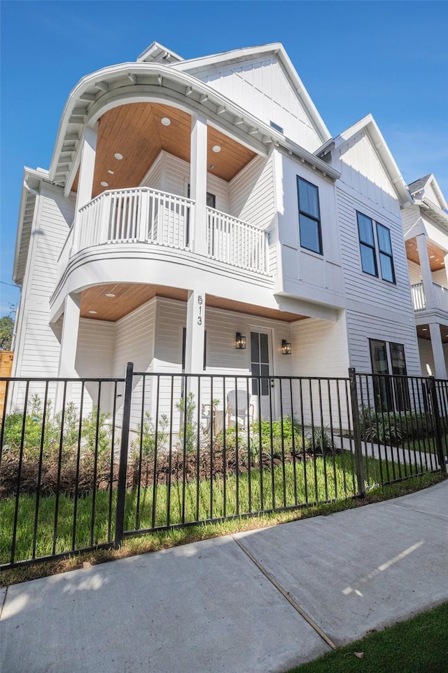 view of front of house with board and batten siding, a fenced front yard, and a balcony