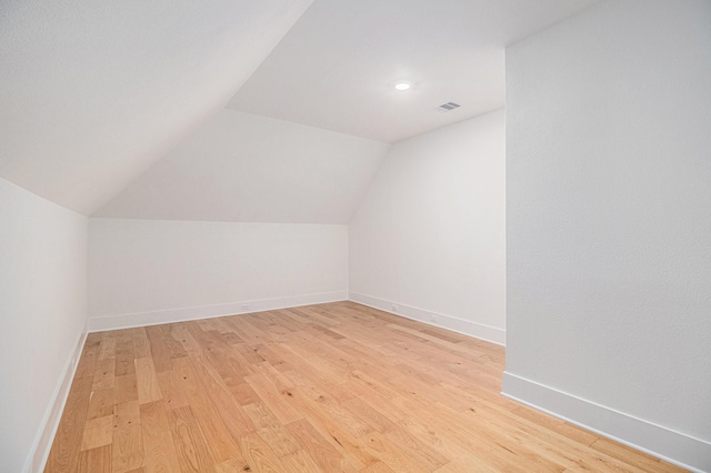 additional living space featuring light wood-style floors, visible vents, vaulted ceiling, and baseboards