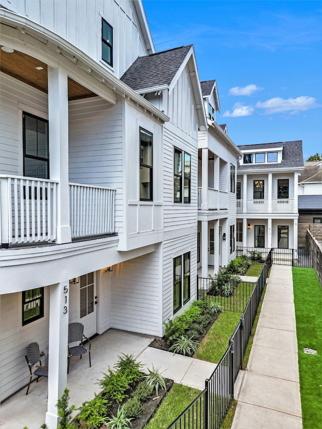 exterior space with board and batten siding, a patio area, fence, and a shingled roof