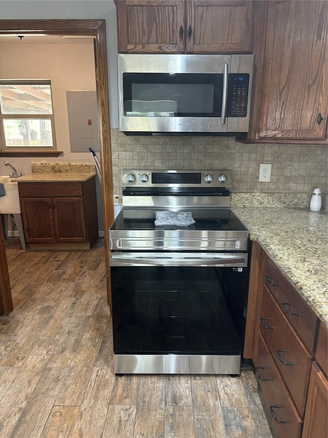 kitchen featuring stainless steel appliances, wood finished floors, backsplash, light stone countertops, and electric panel