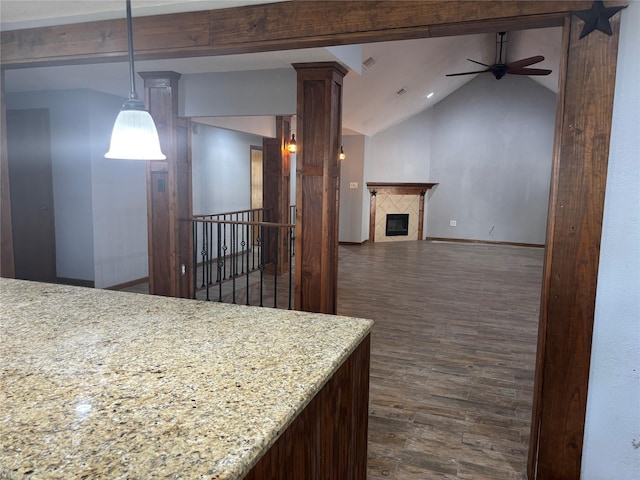 kitchen featuring dark wood-style floors, decorative columns, a tiled fireplace, a ceiling fan, and vaulted ceiling