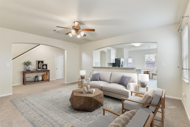 carpeted living area with ceiling fan, baseboards, visible vents, and arched walkways