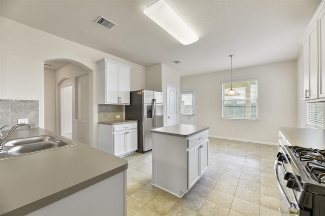 kitchen featuring arched walkways, decorative backsplash, a center island, stainless steel appliances, and a sink