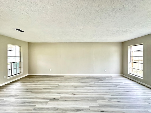 unfurnished room with a textured ceiling, wood finished floors, visible vents, and baseboards