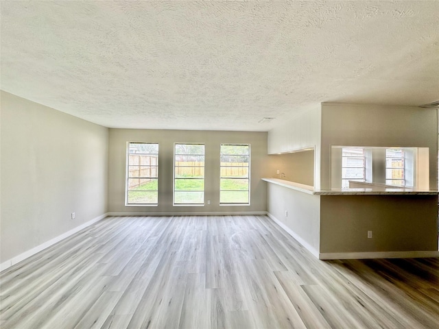 unfurnished living room with a textured ceiling, baseboards, and wood finished floors