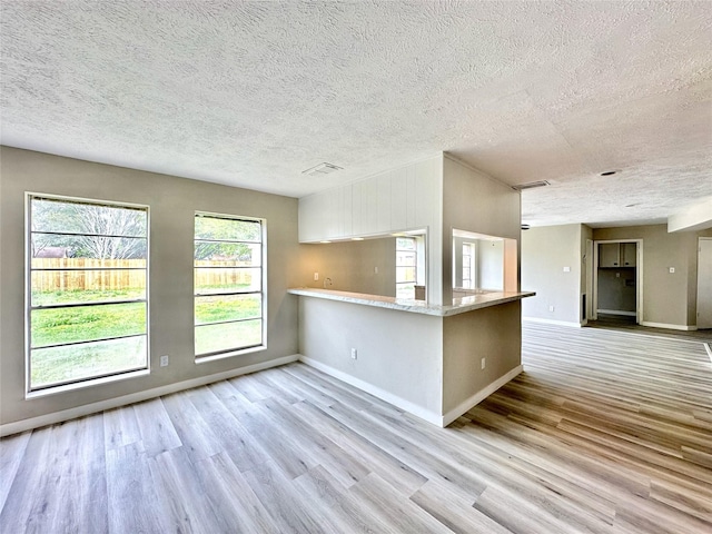 kitchen with a peninsula, visible vents, baseboards, and wood finished floors