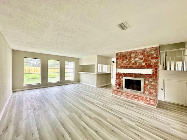 unfurnished living room featuring a textured ceiling, light wood-style flooring, a fireplace, visible vents, and baseboards