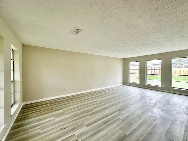 unfurnished room with visible vents, a textured ceiling, baseboards, and wood finished floors