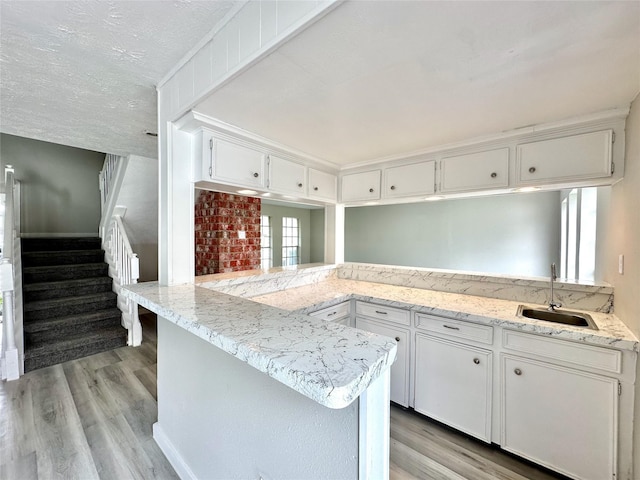 kitchen featuring light wood-type flooring, white cabinetry, a sink, and a peninsula