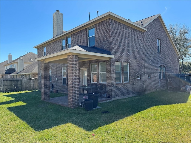 rear view of house featuring a yard, brick siding, a chimney, and fence