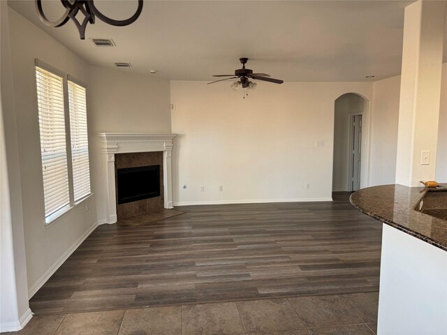 unfurnished living room with visible vents, arched walkways, ceiling fan, and a tiled fireplace