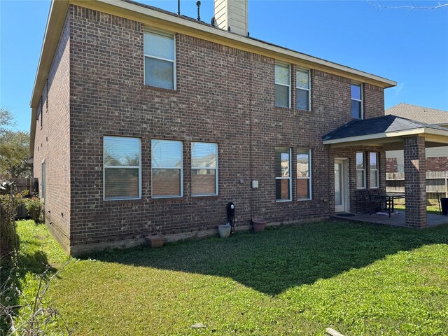 back of property with brick siding, a patio, a chimney, and a yard