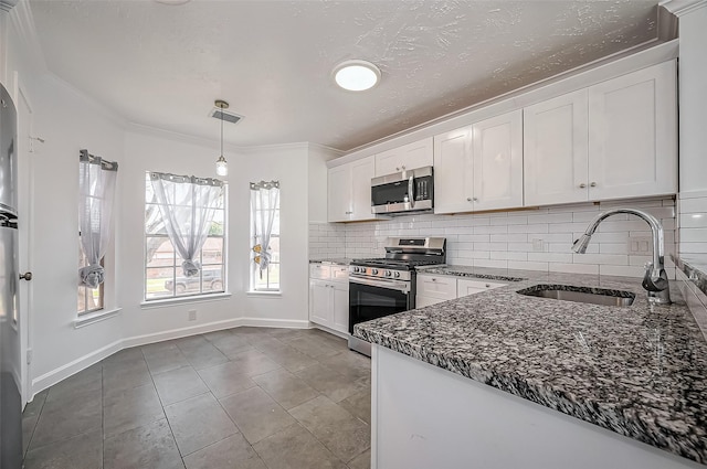 kitchen with a sink, white cabinets, appliances with stainless steel finishes, decorative backsplash, and dark stone counters