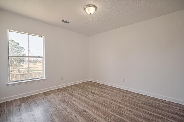 spare room featuring baseboards, a textured ceiling, visible vents, and wood finished floors