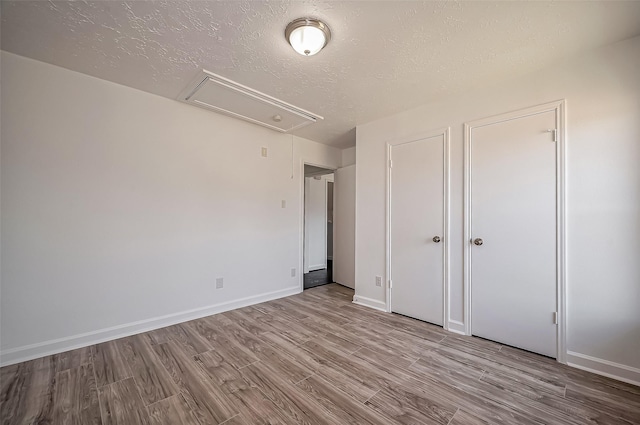 unfurnished bedroom with attic access, a textured ceiling, baseboards, and wood finished floors