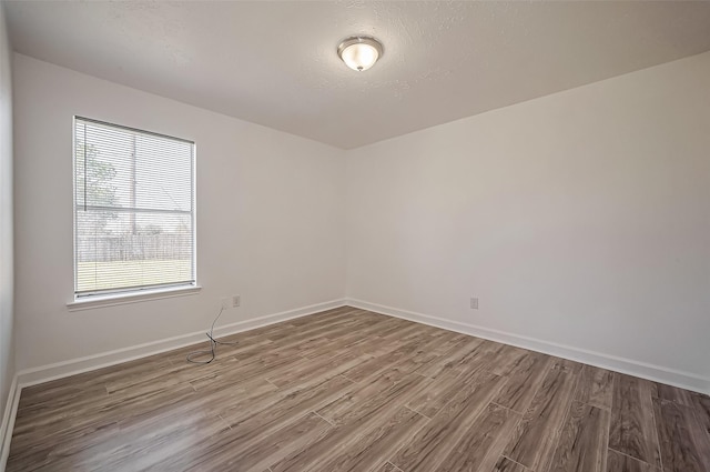 empty room with a textured ceiling, baseboards, and wood finished floors