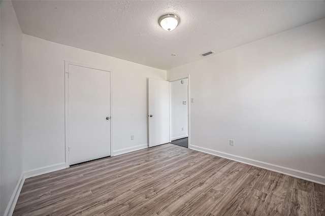 unfurnished bedroom with a textured ceiling, wood finished floors, visible vents, and baseboards