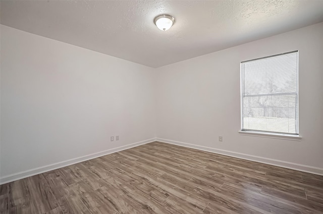 unfurnished room with a textured ceiling, baseboards, and wood finished floors