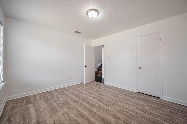 spare room with baseboards, visible vents, wood finished floors, stairs, and a textured ceiling