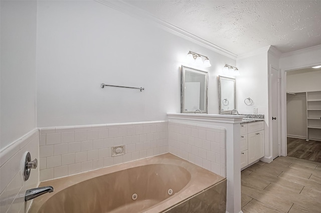 full bath with a textured ceiling, wood finished floors, vanity, ornamental molding, and a jetted tub