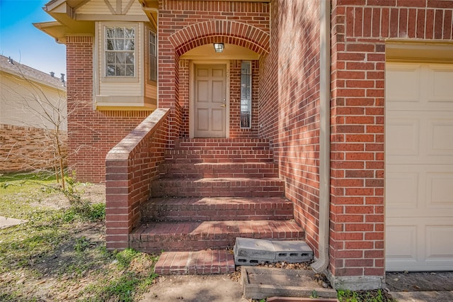 view of exterior entry featuring a garage and brick siding